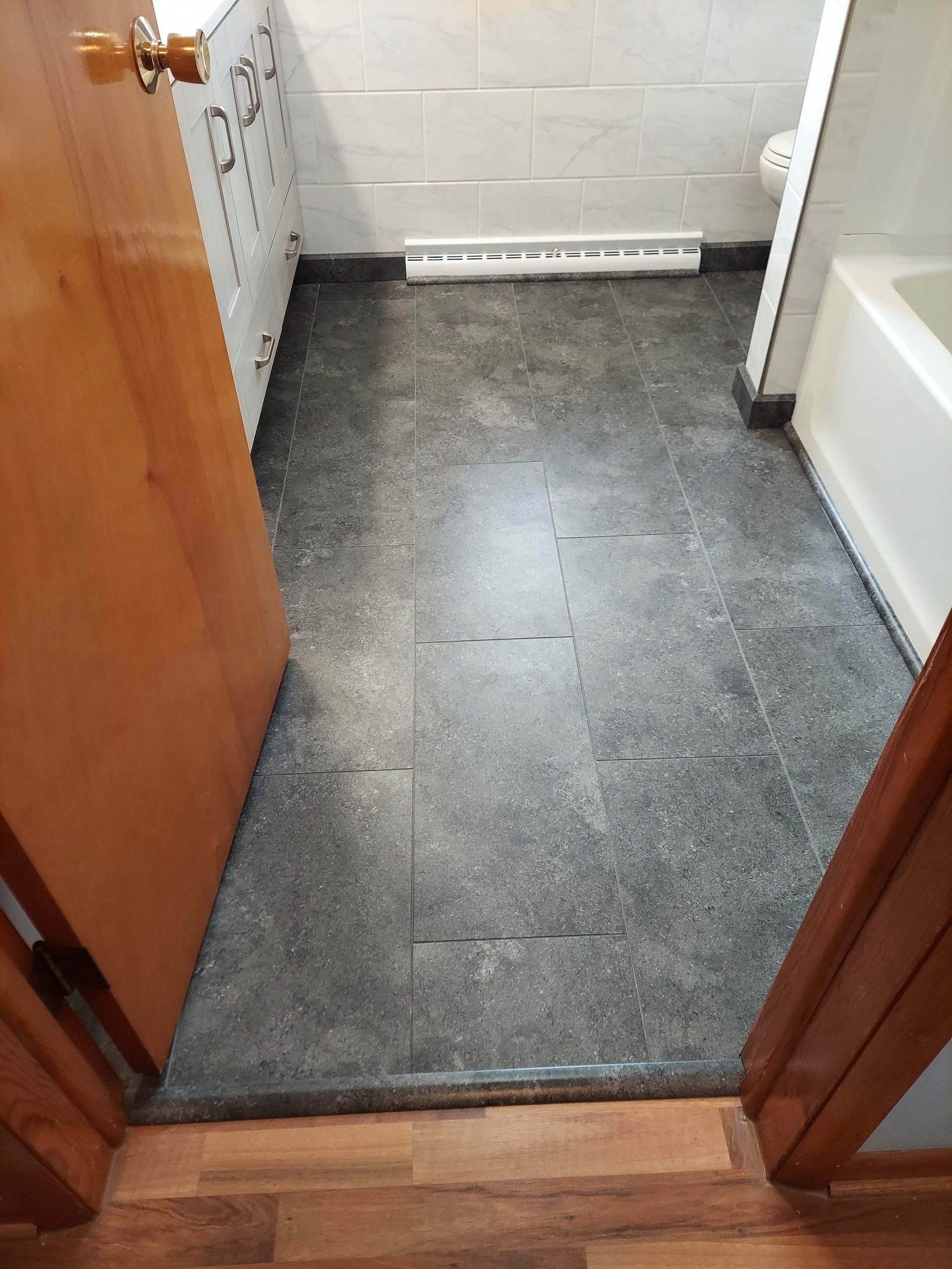 A bathroom with a black tile floor and a bathtub.