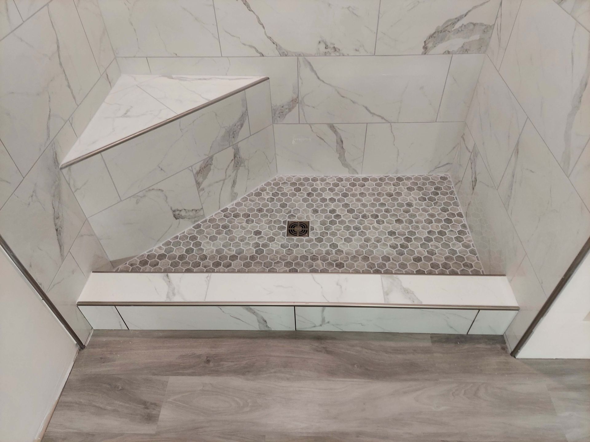 A shower stall with a corner shelf and a drain.