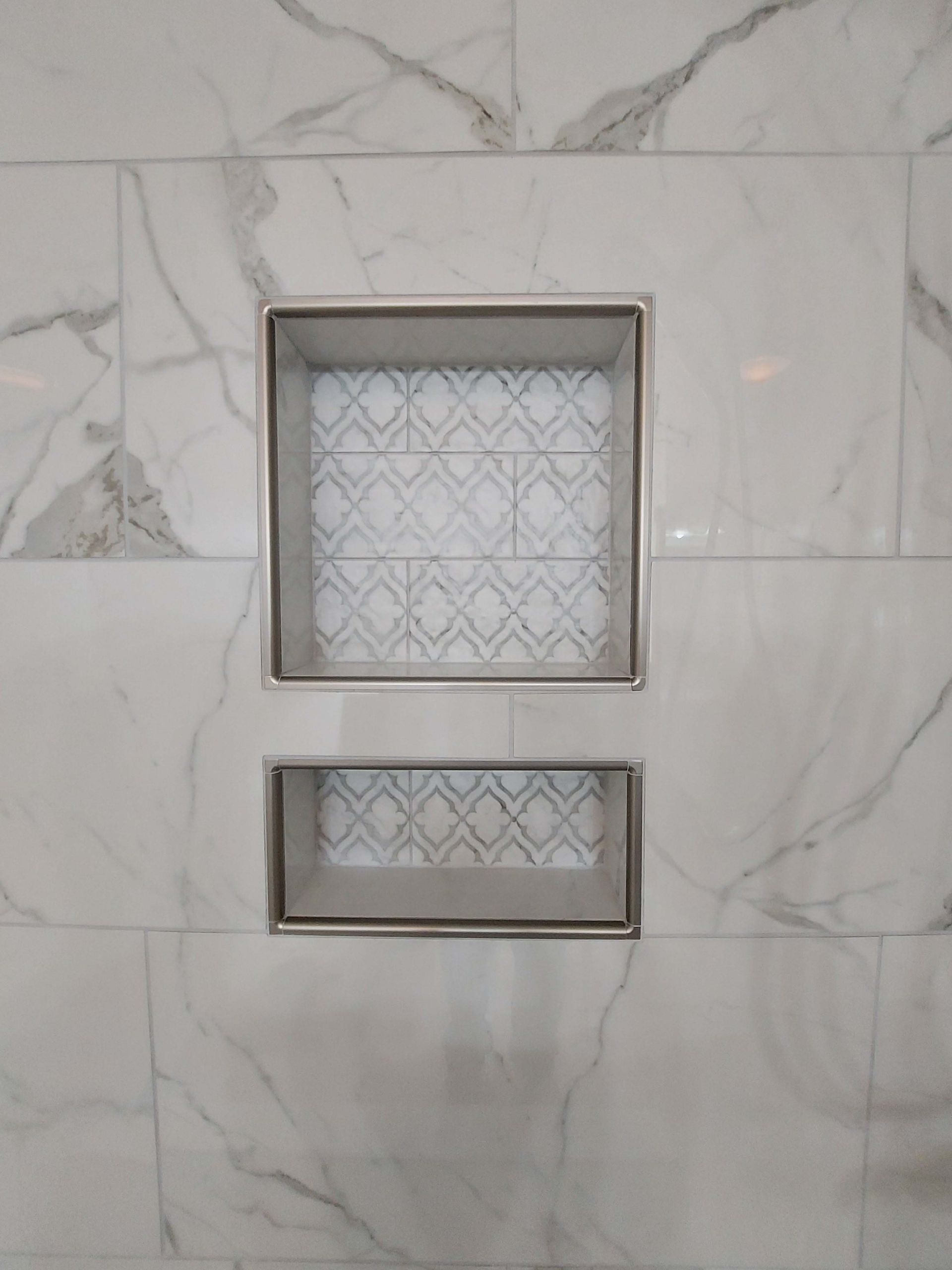A shower niche in a bathroom with marble tiles and a stainless steel frame.