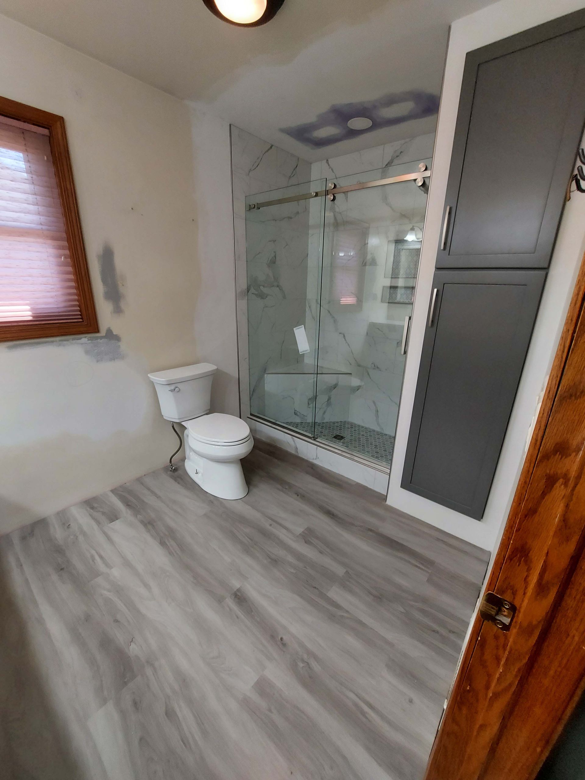 A bathroom with a toilet , shower and cabinets.