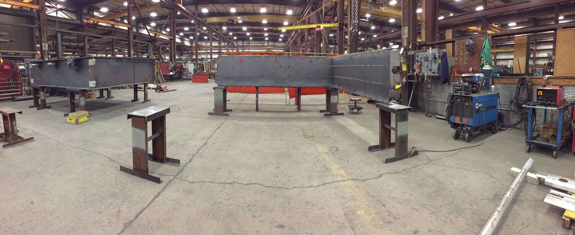 Industrial workshop with large metal structures on stands. Overhead lighting illuminates the space.