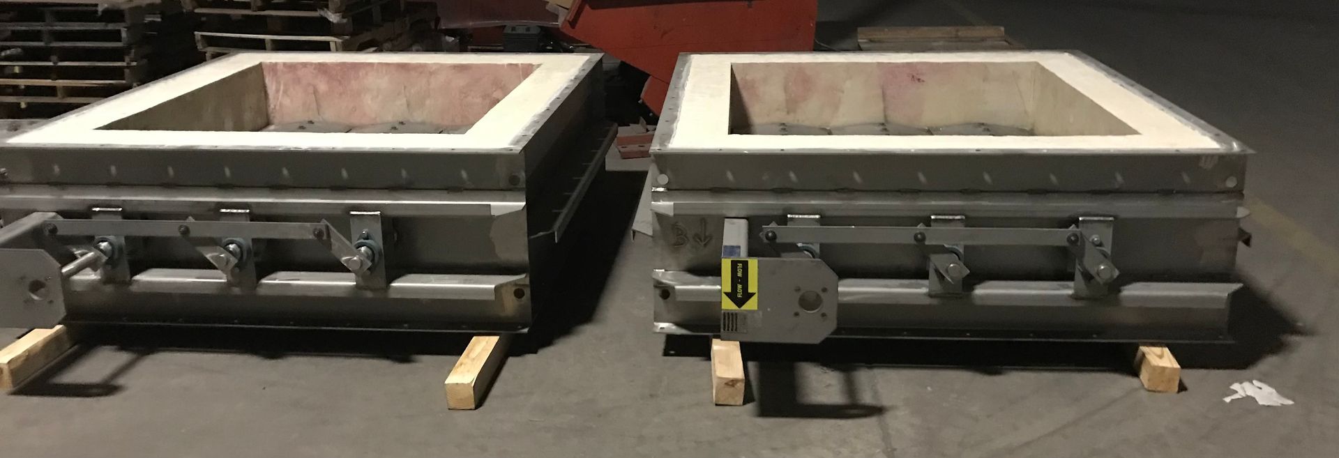 Two large, square industrial containers, side-by-side, sitting on wooden blocks.