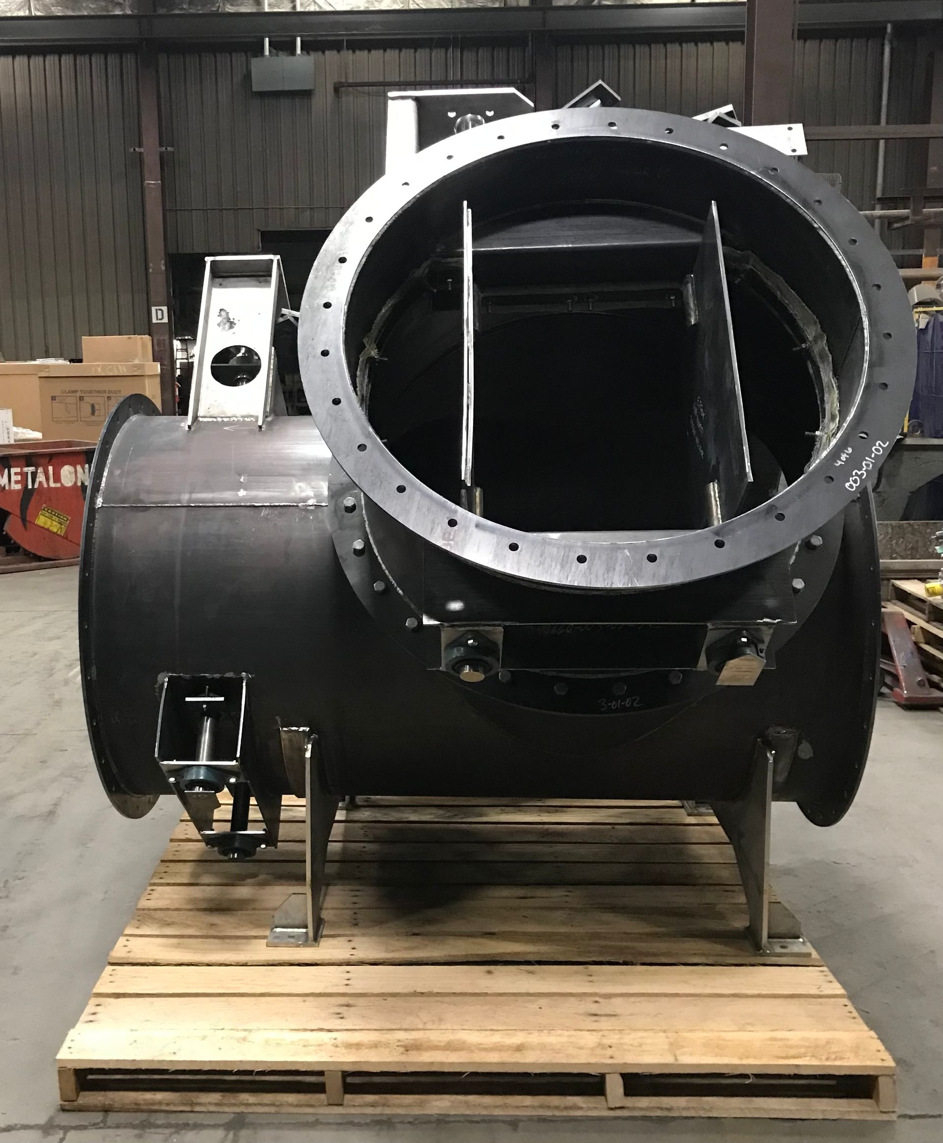 Large, black industrial valve on a wooden pallet, with circular openings and flange bolt holes.