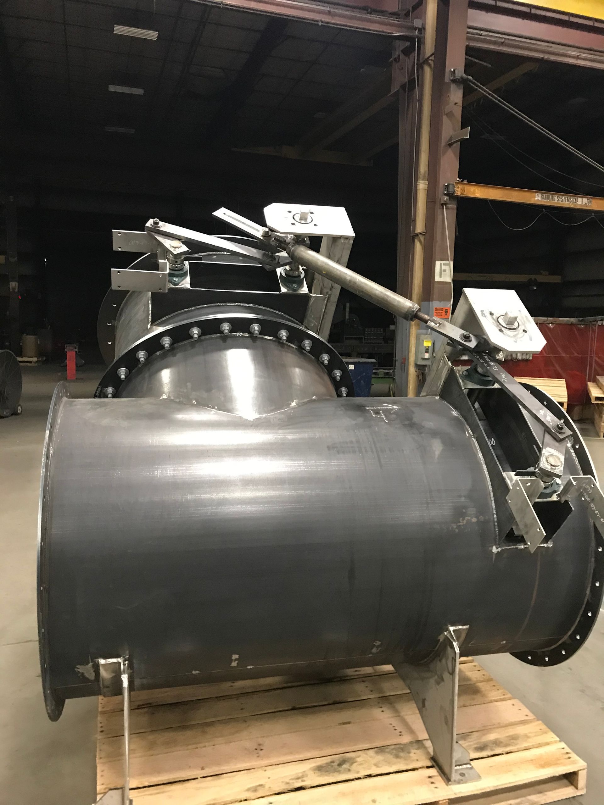 Large industrial valve with attached actuators, black and silver, in a warehouse setting.