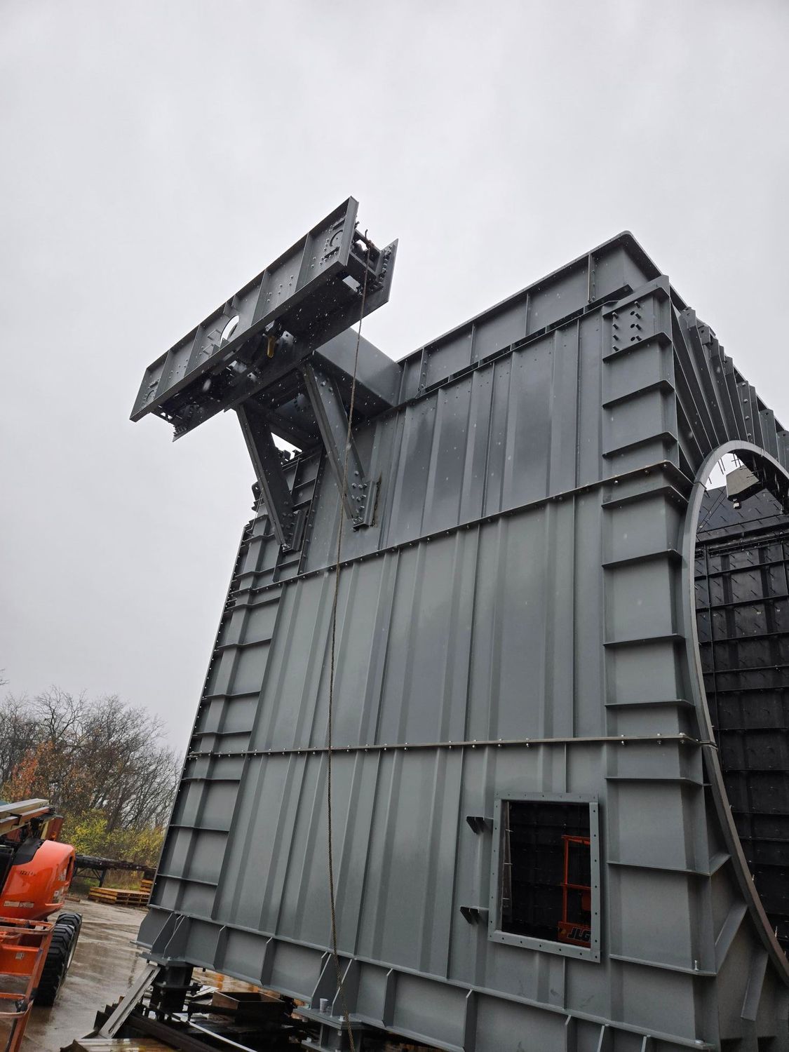 Large, gray industrial structure with an angled top section and a rectangular window, outdoors.