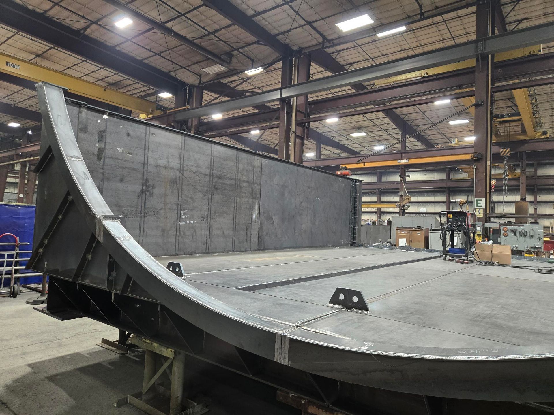 Large, curved metal structure in a workshop; grey metal with rivets.