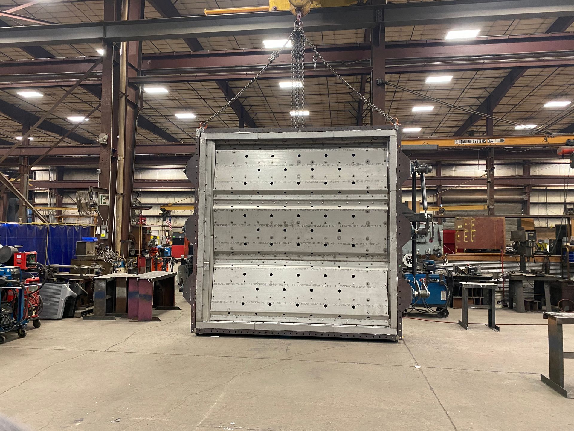 Large metal box suspended from a crane inside a workshop, with various tools and equipment in the background.