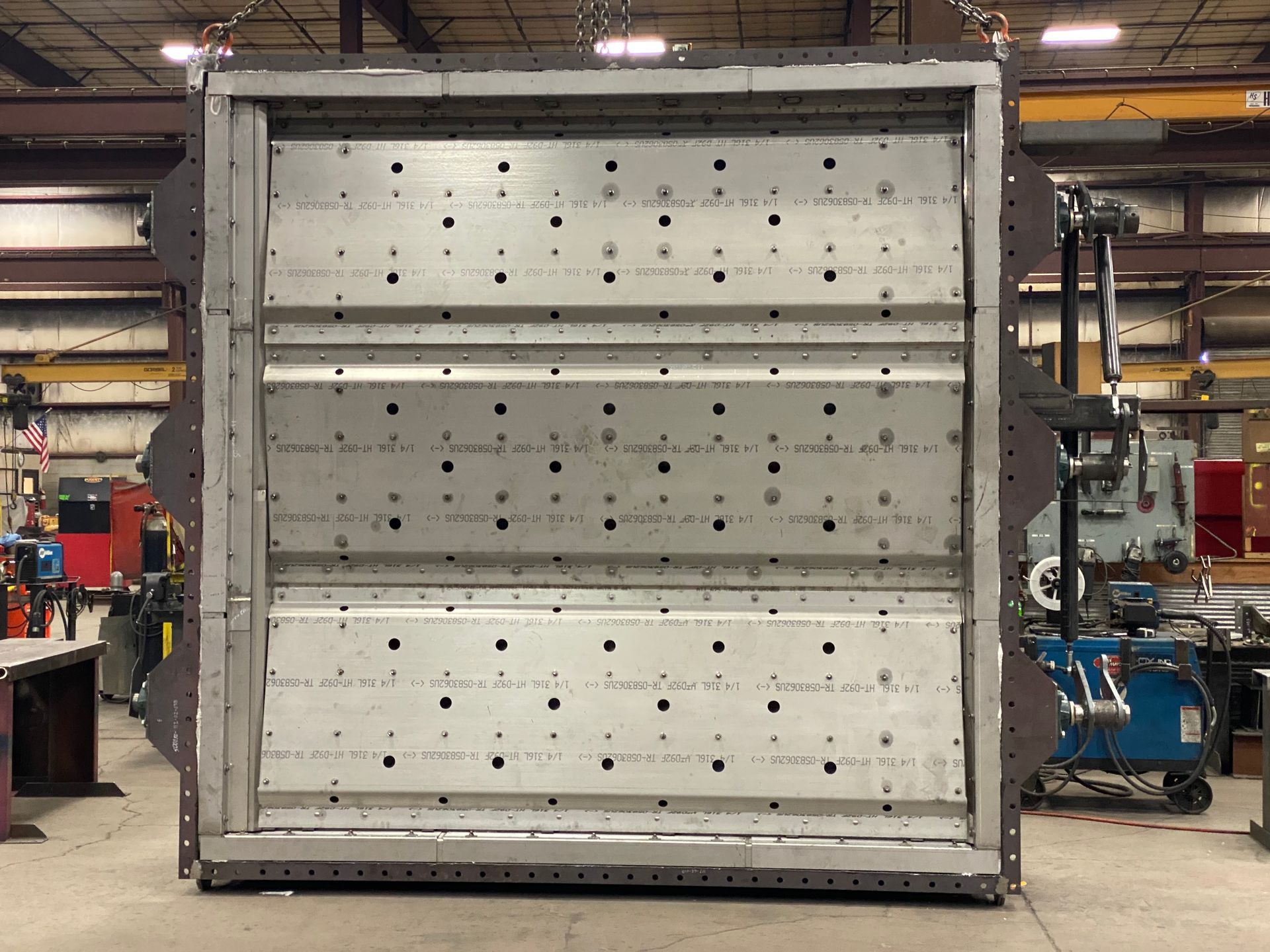 Large, rectangular metal structure with three rows of openings; suspended from above in a workshop.