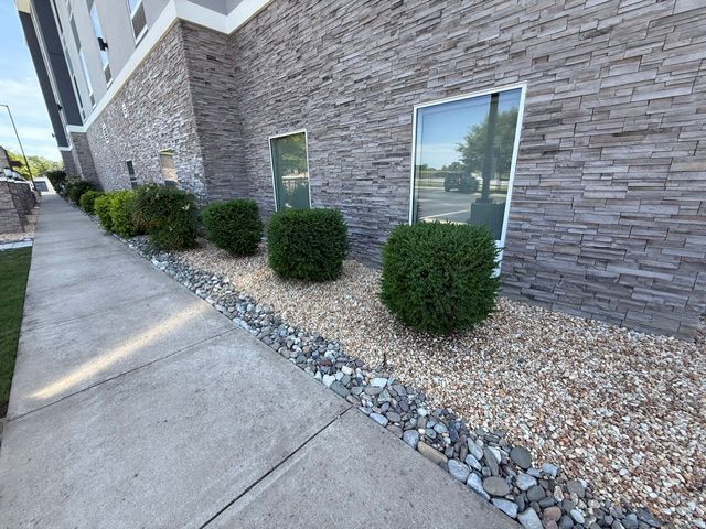 A sidewalk with bushes and rocks in front of a building