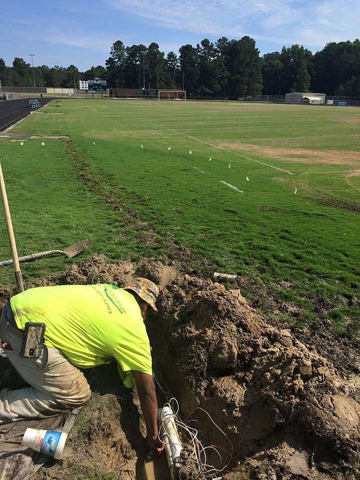 A man is digging a hole in the dirt in front of a soccer field.