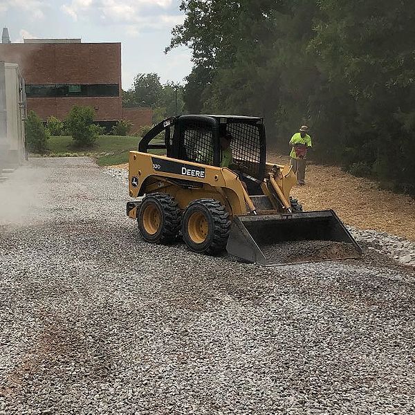 A yellow and black skid steer is driving down a gravel road.