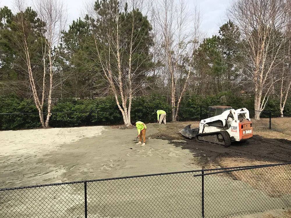 Two men are working on a dirt field next to a bulldozer.