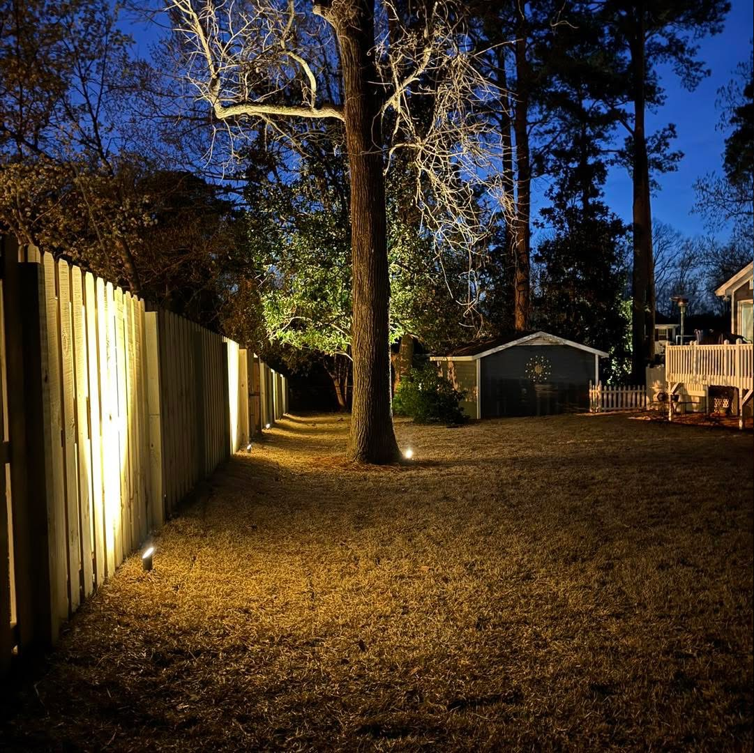 A wooden fence is lit up at night in a backyard