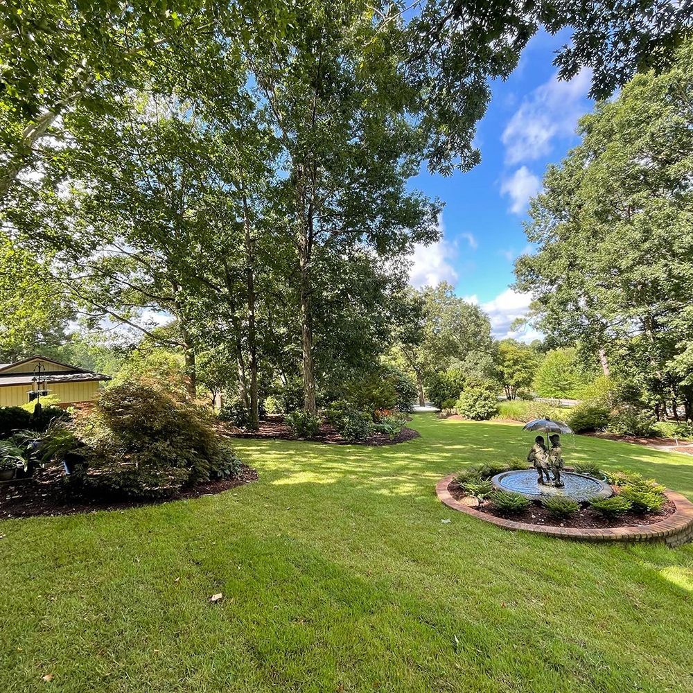A large lush green lawn with a fountain in the middle of it surrounded by trees.