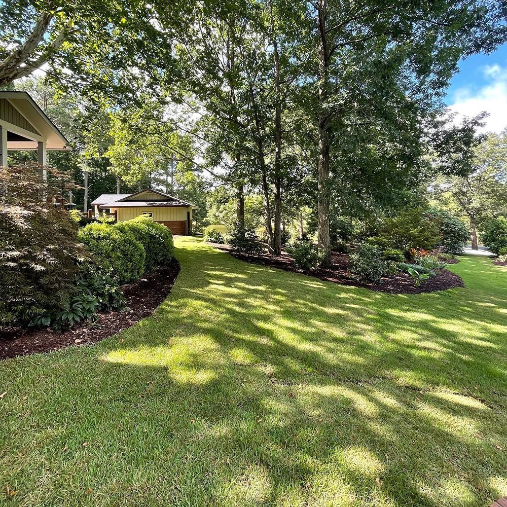 A large lush green lawn with trees in the background and a house in the background.