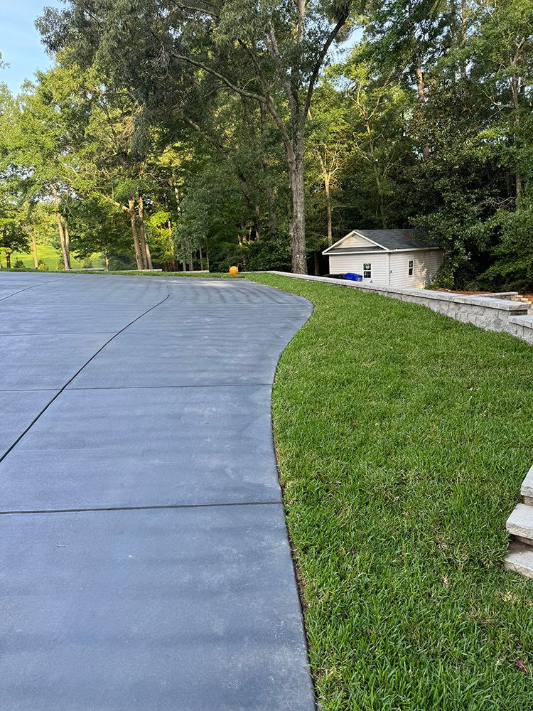 A concrete driveway leading to a house surrounded by grass and trees.