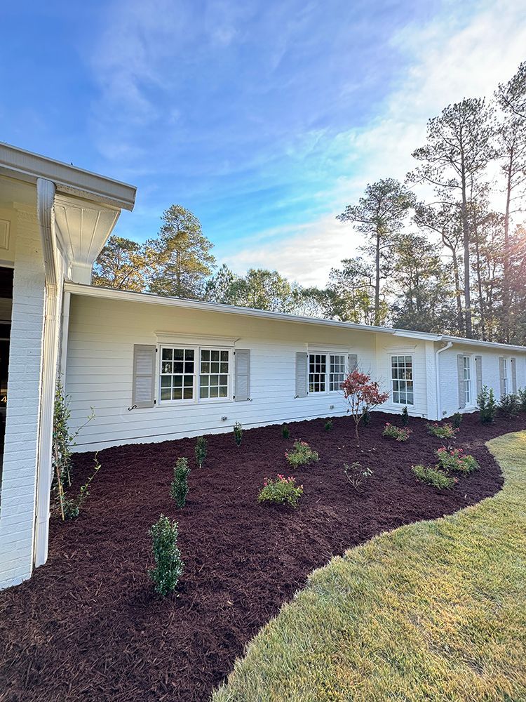 A white house with a lot of windows and mulch in front of it.