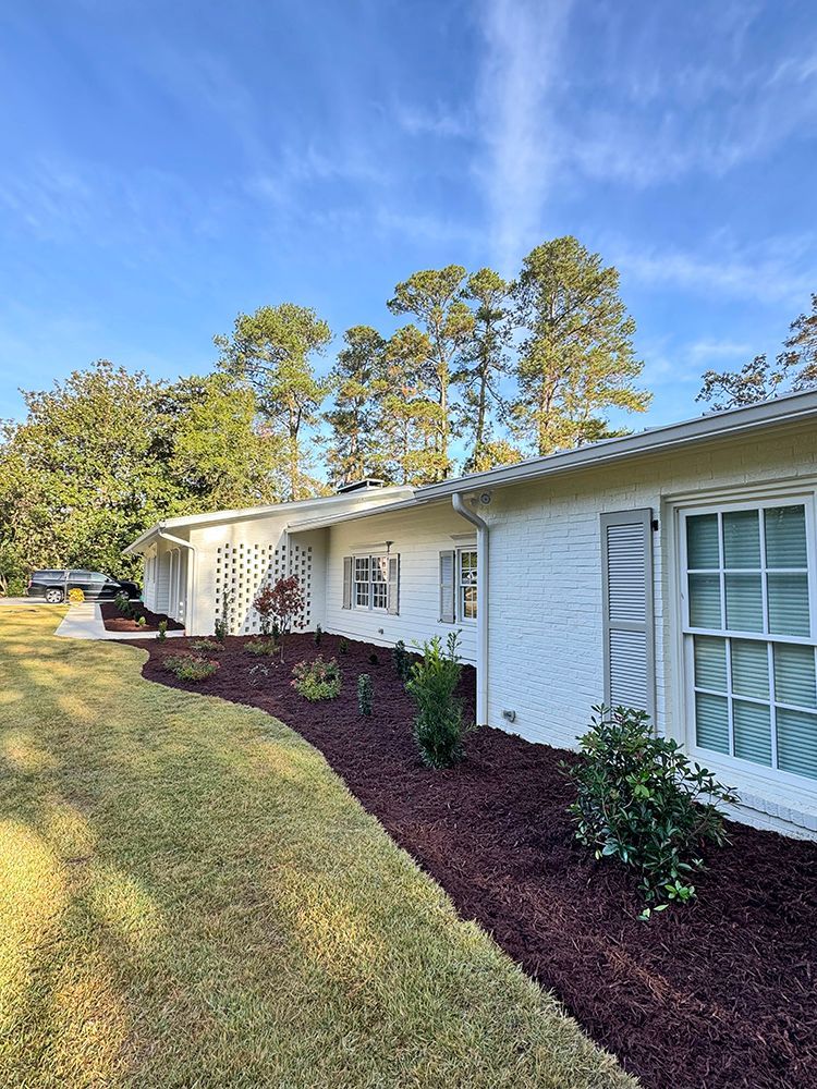 A white brick house with a lot of windows and mulch in front of it.