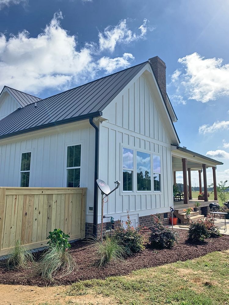 A white house with a black roof and a wooden fence in front of it.