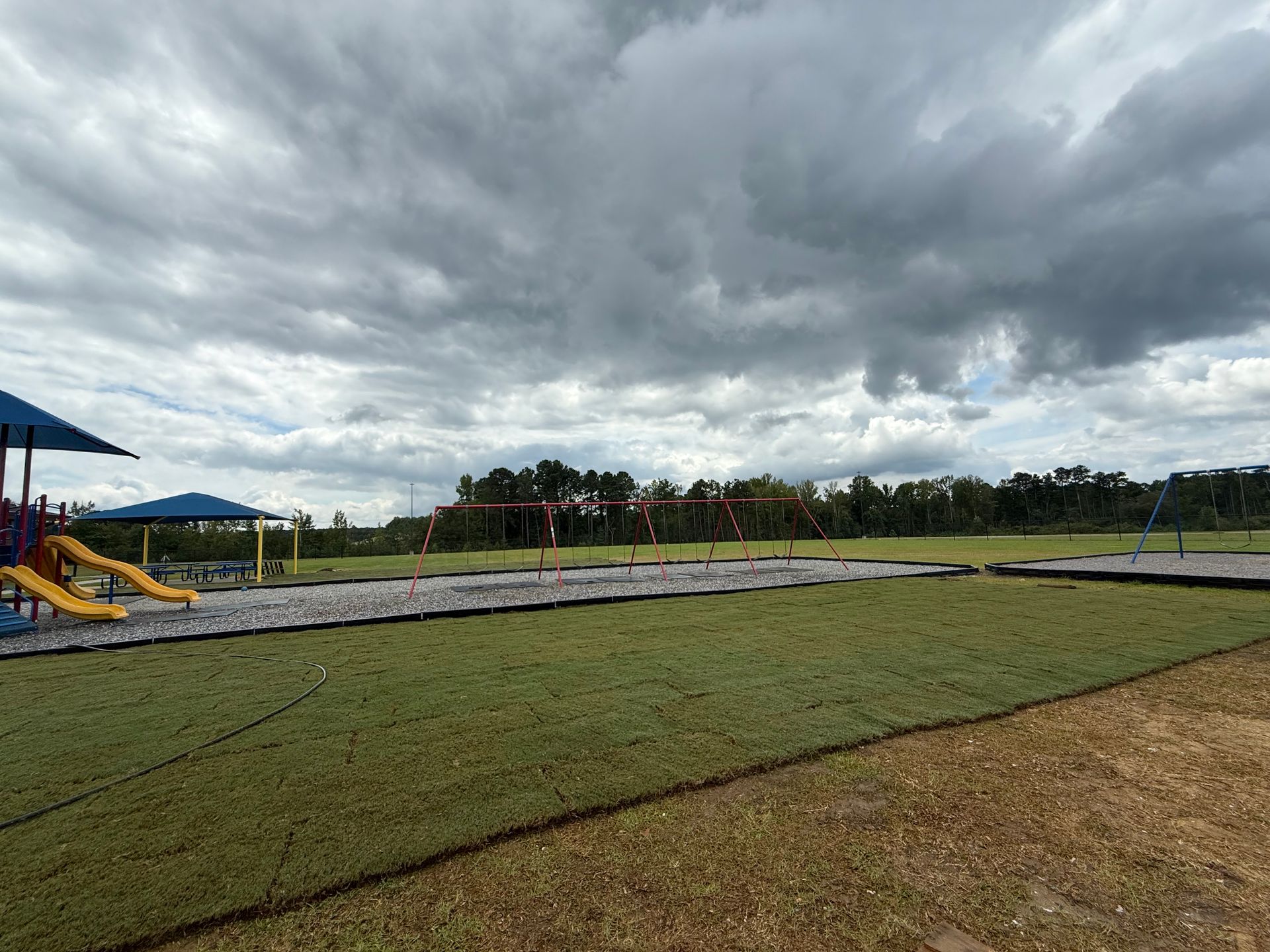 Playground with slides, swings, and new sod under cloudy sky.