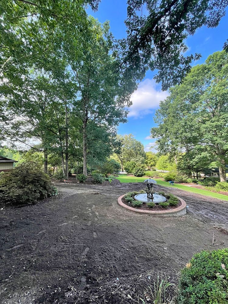 There is a fountain in the middle of the yard surrounded by trees.