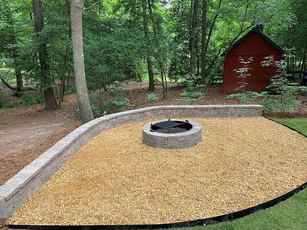 A fire pit is surrounded by gravel and a wall in a backyard.