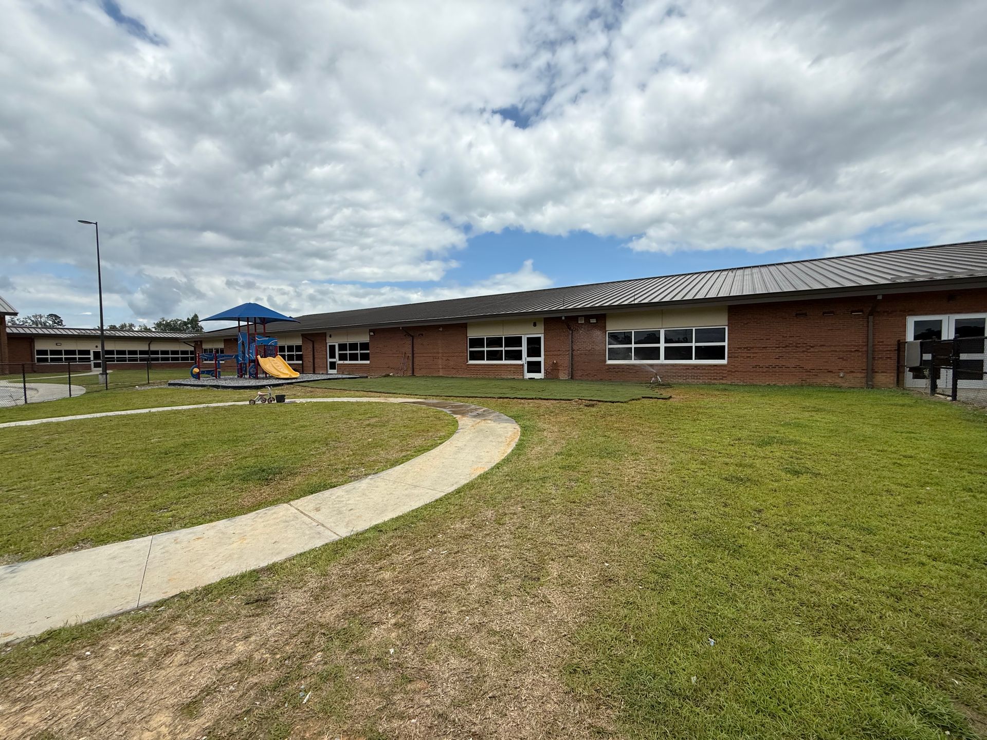 A brick school building with a playground on a cloudy day. A paved walkway leads to the building.