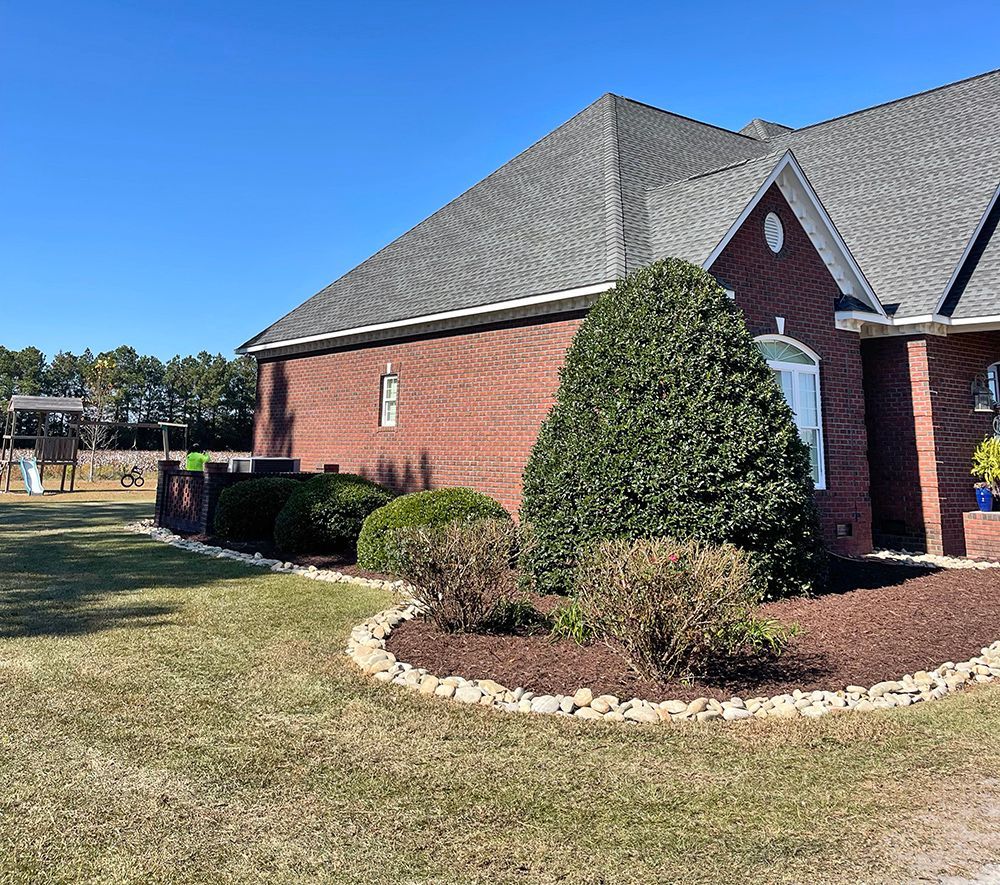 A brick house with a gray roof and a lush green lawn in front of it.