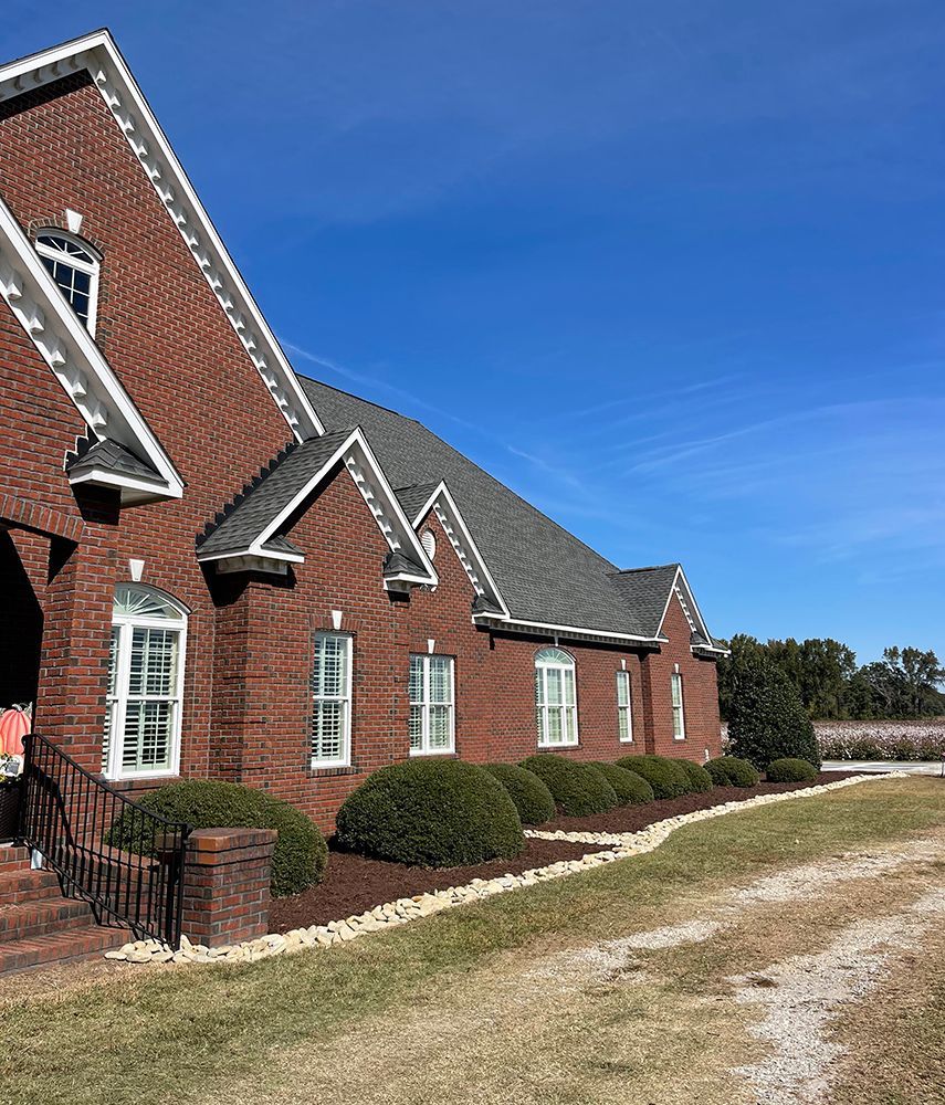 A large brick house with a gray roof is sitting in the middle of a grassy field.