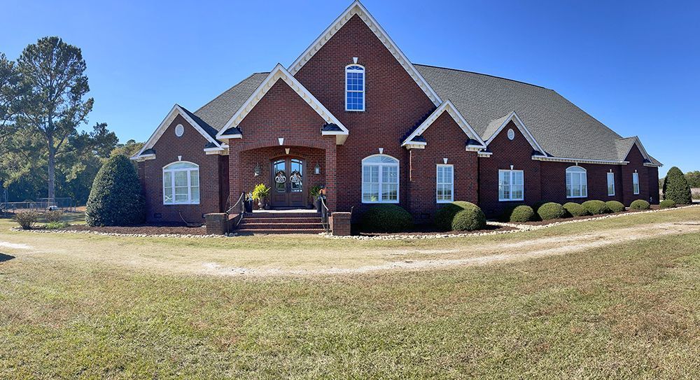 A large brick house is sitting on top of a lush green field.