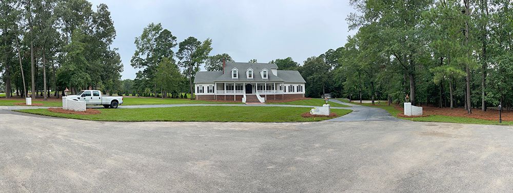 A white truck is parked in front of a large house surrounded by trees.