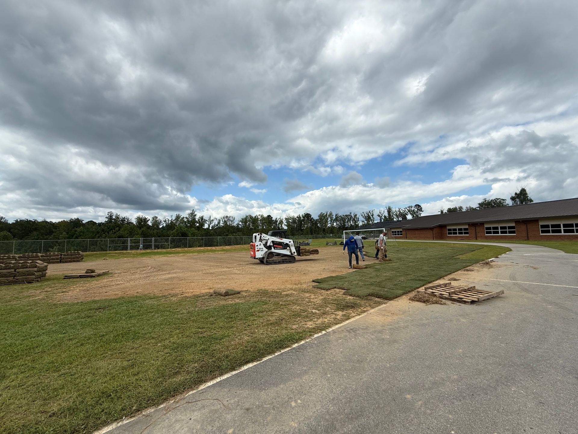 Construction site with a small bulldozer, workers, and a building under a cloudy sky.
