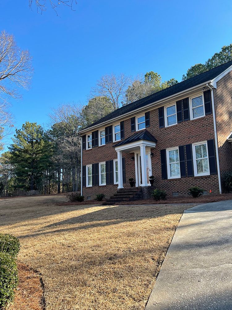 A large brick house with black shutters and a large driveway.