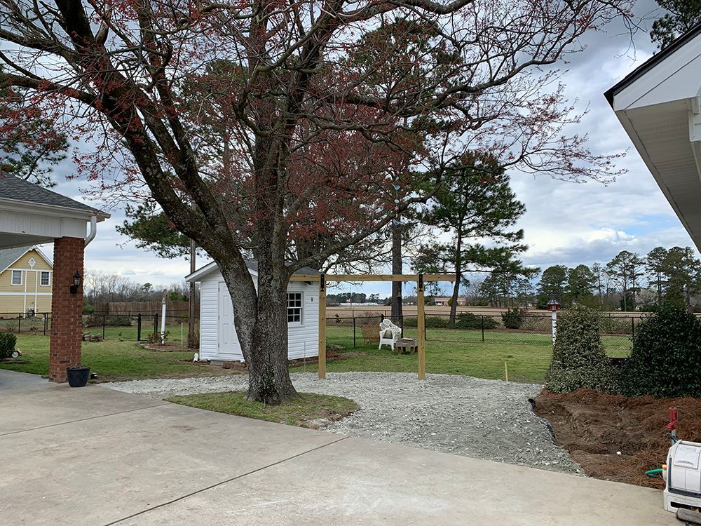 A driveway leading to a house with a shed and a tree.