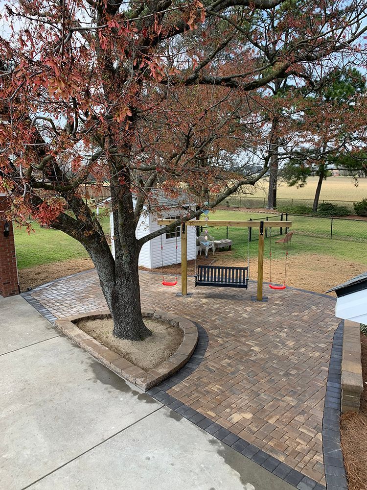 A patio with a swing set and a tree in the middle of it.