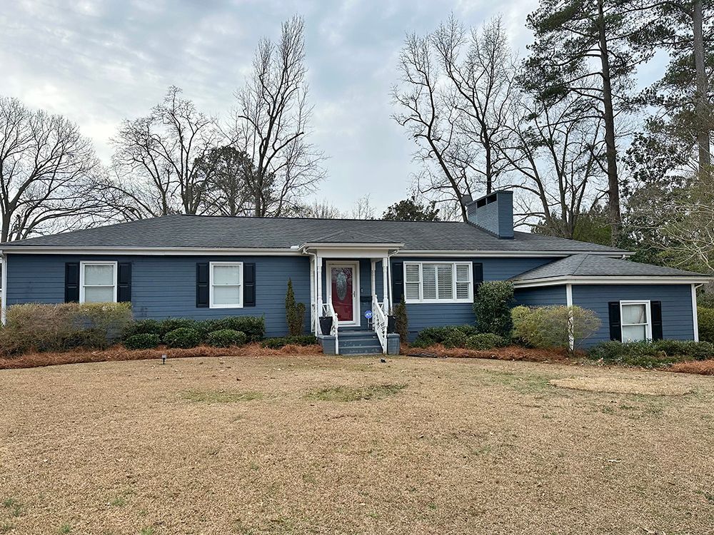 A blue house with black shutters and a red door is sitting on top of a dirt field.