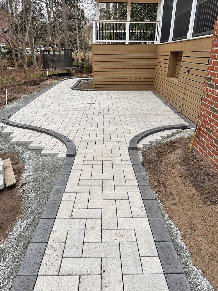 A brick walkway leading to a patio with a screened in porch.