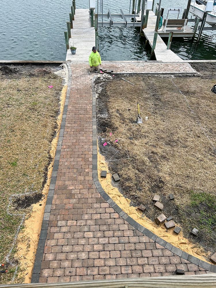 A man is kneeling on a brick walkway next to a dock.