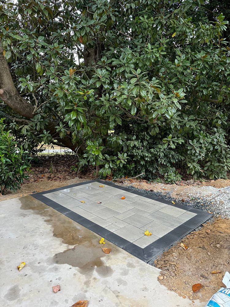 A concrete patio with a black border is surrounded by trees.