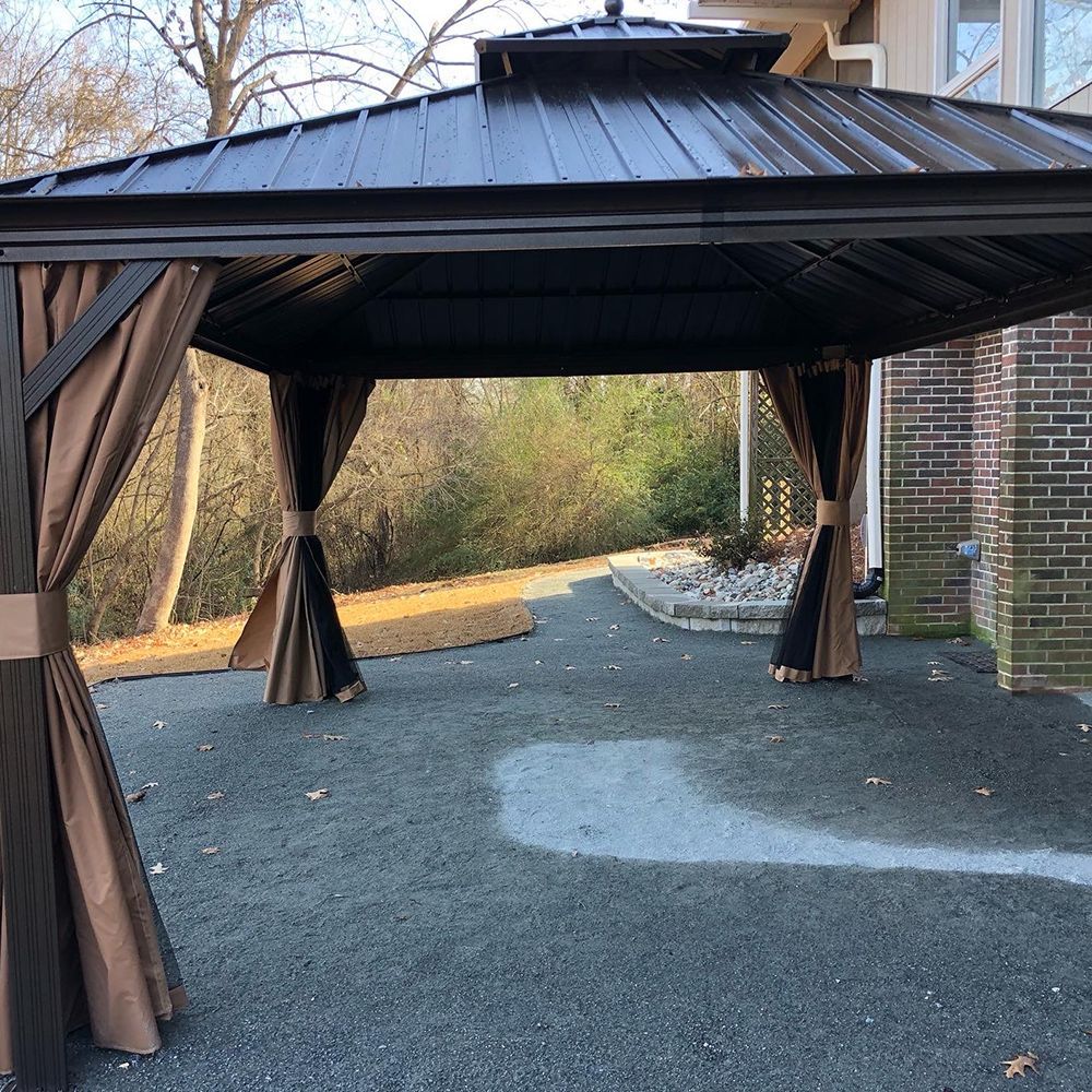 A gazebo with brown curtains is sitting in front of a brick house.
