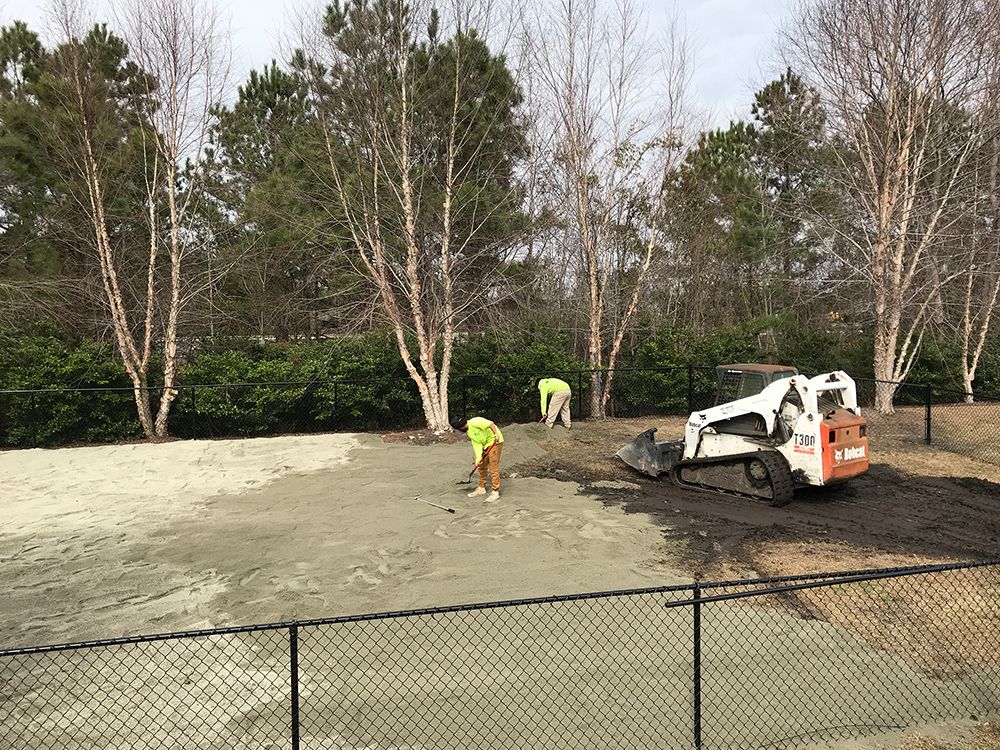A bulldozer is working on a dirt field next to a chain link fence.