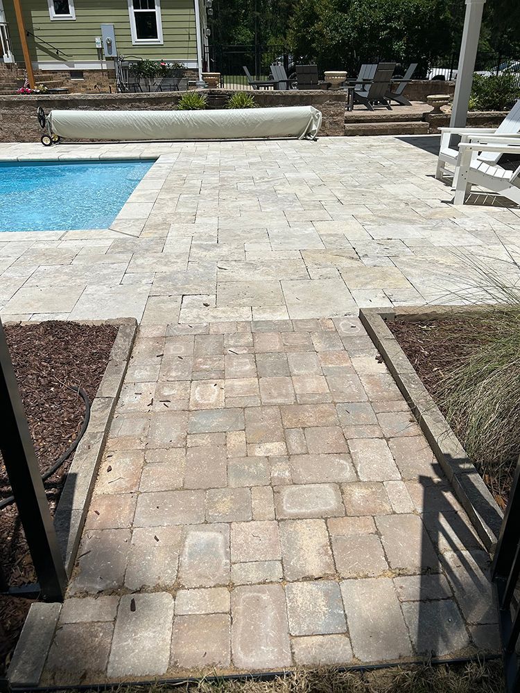 A patio with a pool in the background and a walkway leading to it.