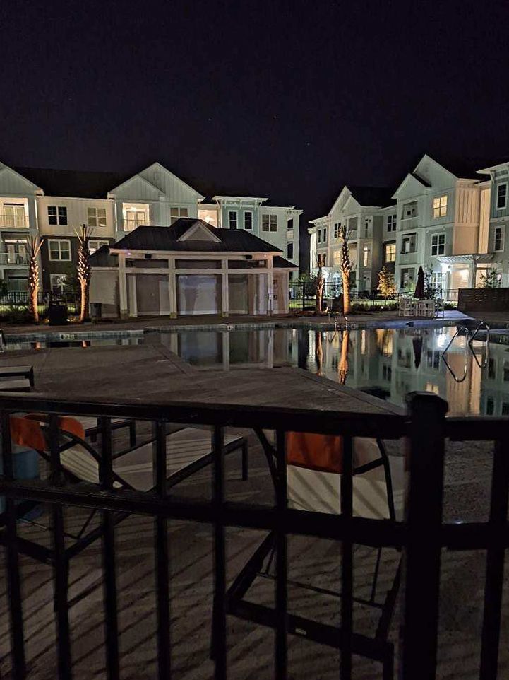 A large swimming pool is surrounded by buildings at night