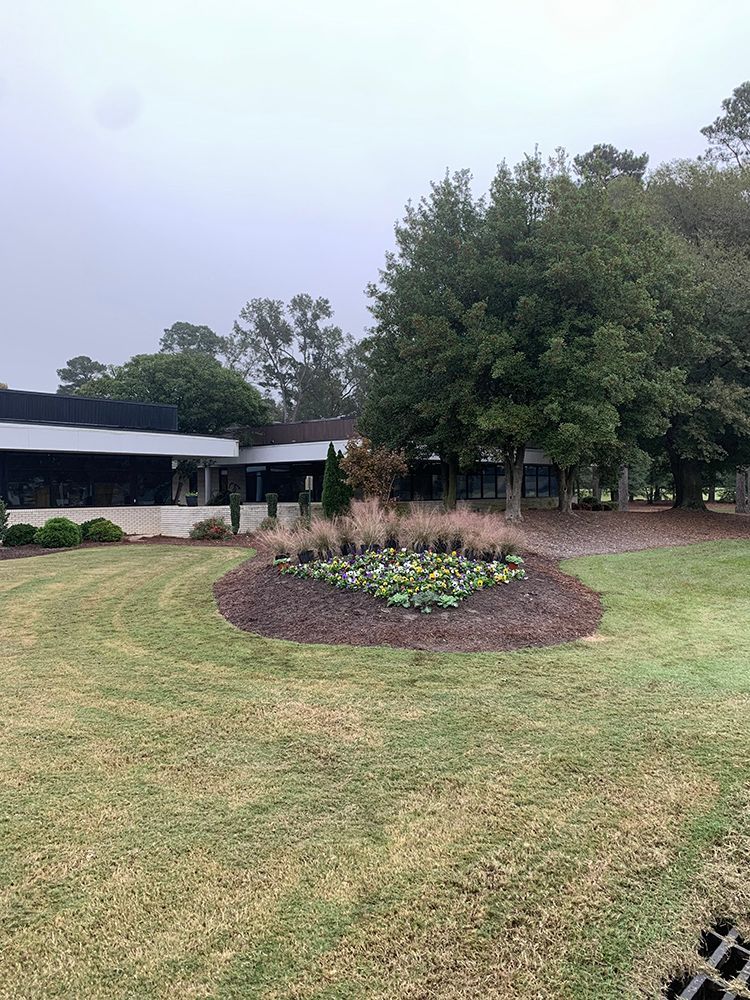 A large lawn with a circle of flowers in the middle of it in front of a building.
