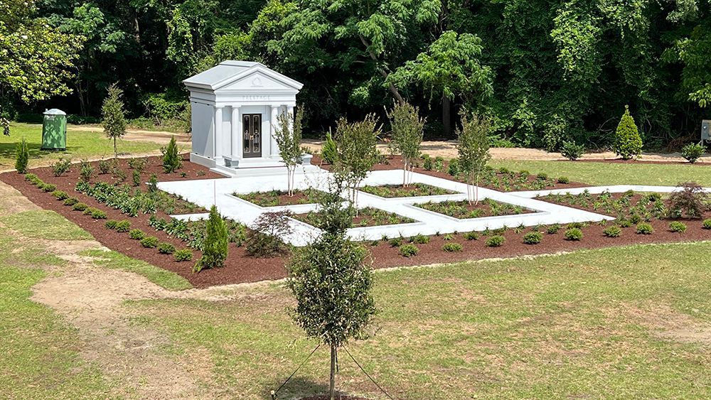 A small white building in the middle of a grassy field surrounded by trees.