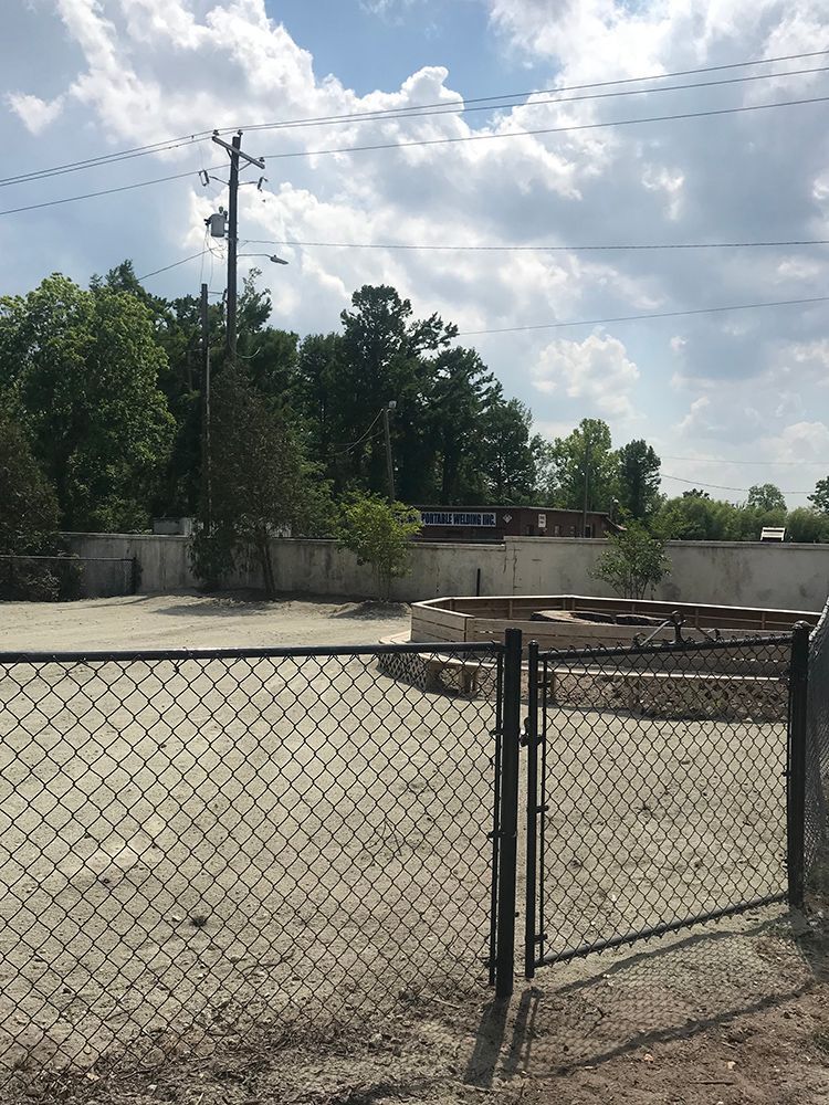 A chain link fence surrounds a dirt area with trees in the background