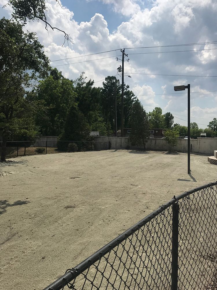 A chain link fence surrounds a dirt field with trees in the background
