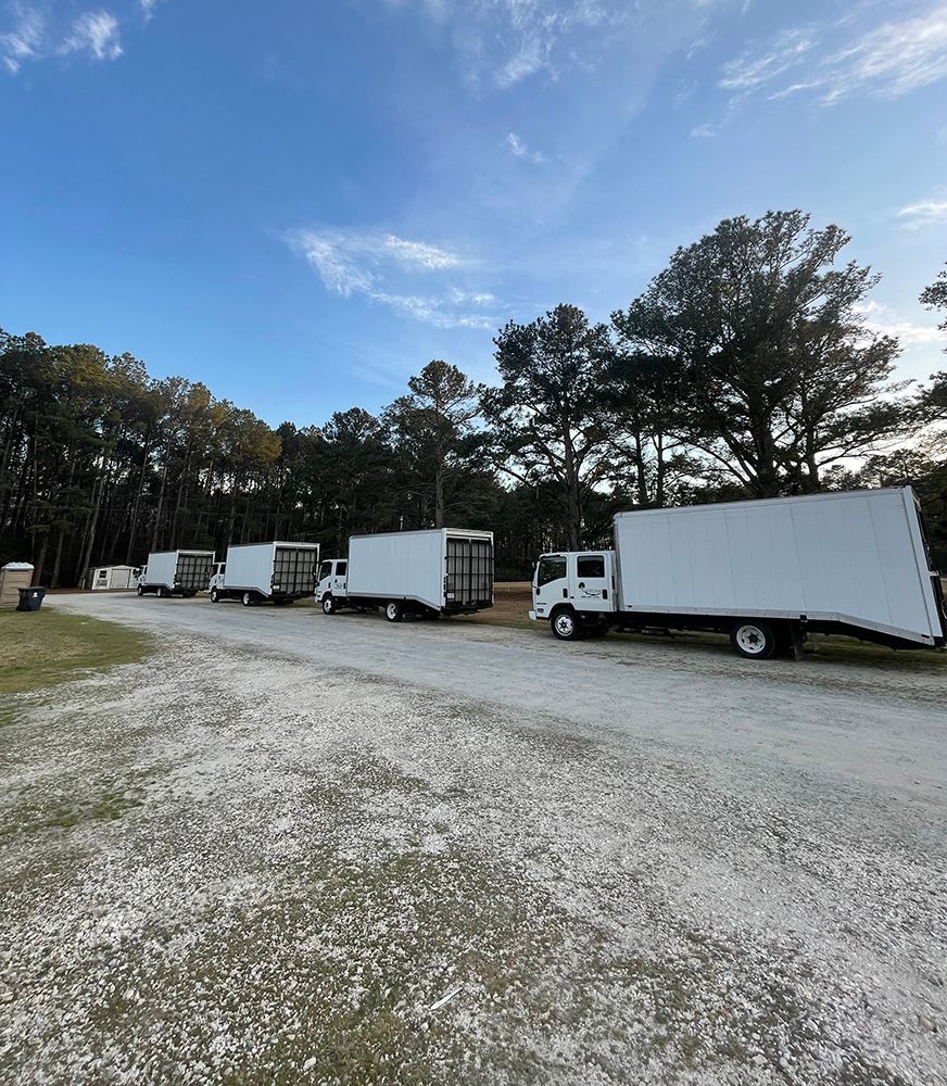 A row of white trucks are parked in a gravel lot