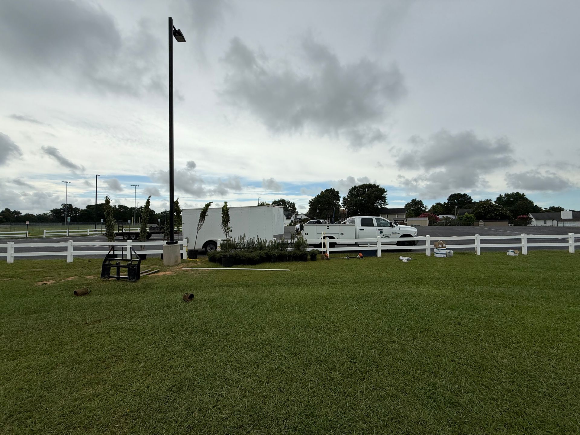 A white truck is parked in a grassy field next to a white fence.