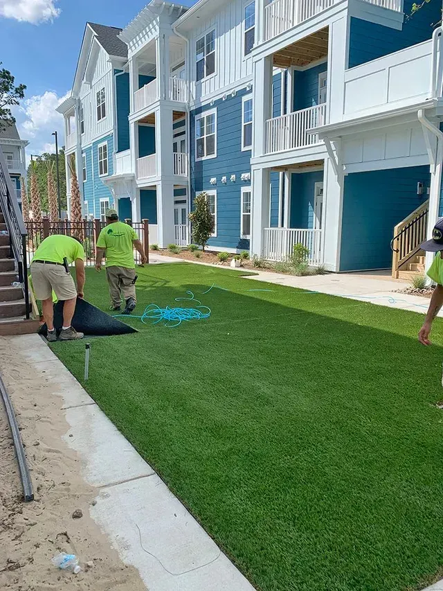 A group of men are working on a lawn in front of a building.